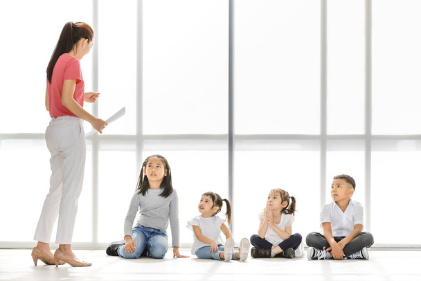 Asyalı Öğretmen Asyalı çocuklar için bir şey öğretmek, çocuklar onu dinlemek dikkat, büyük beyaz pencere önünde oturuyorlar. - Fotoğraf, Görsel