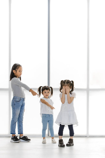 Aziatische kinderen wijzen op Aziatisch meisje, de tribune naast grote witte venster. - Foto, afbeelding
