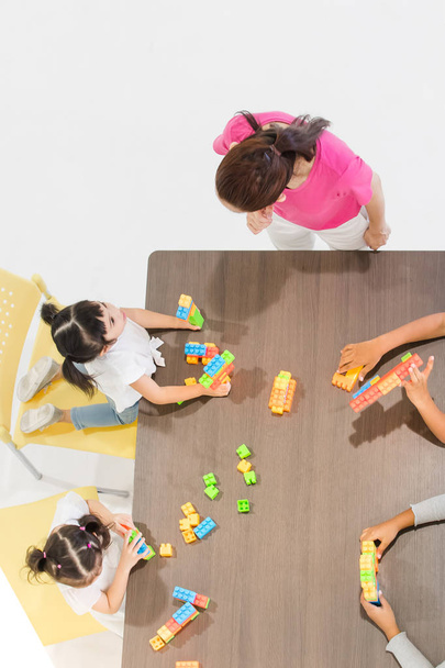 Group of kids and teacher playing colorful toys in classroom. Concept for happy and funny learning, brain development activities in school free time. - Photo, image