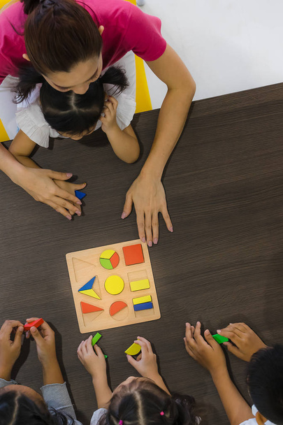 Flat lay shot of Asian teacher play  geometry blocks toy with Asian student together, concept for classroom. - Photo, image