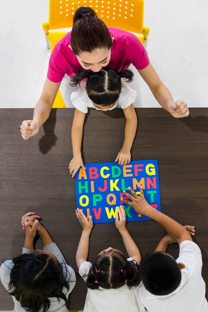 Flat lay shot de professores asiáticos jogar colorido alfabeto puzzle brinquedo com estudantes asiáticos juntos, conceito para sala de aula
. - Foto, Imagem