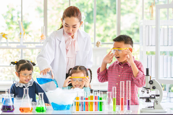 Naturwissenschaftler unterrichten asiatische Schüler über Chemikalien, Lehrer gießen Chemikalien in Glasschale, buntes Reagenzglas und Mikroskop auf Tisch im Laborraum, Konzept für das Lernen im Laborraum. - Foto, Bild