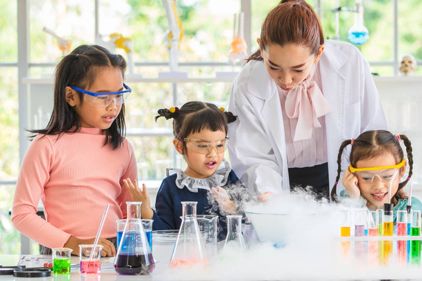 Naturwissenschaftslehrer unterrichten asiatische Schüler über Chemikalien, Rauch schwebt aus dem Blasrohr, buntes Reagenzglas und Mikroskop auf dem Tisch im Laborraum, Konzept für das Lernen im Laborraum. - Foto, Bild