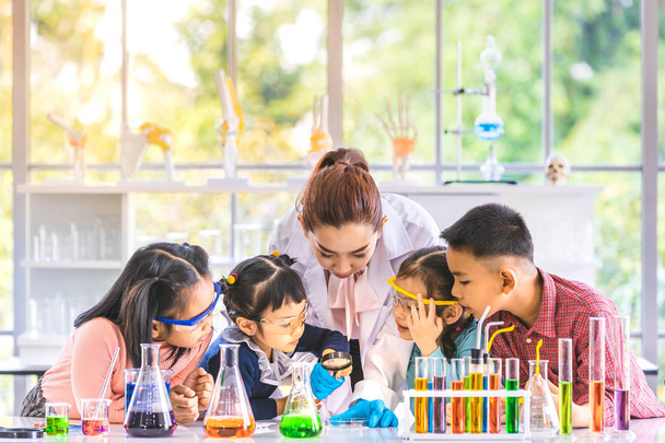 Tudomány tanár tanít ázsiai diákok laboratóriumi szobában, tanár használata nagyítóval kell keresni valamit, színes kémcsőbe, és Mikroszkóp tábla, koncepció a teremben laboratóriumi vizsgálat. - Fotó, kép