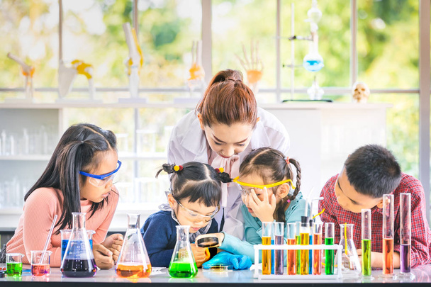 Science teacher teach Asian students in laboratory room, teacher use magnifying glass to look through something, colorful test tube and microscope on table , concept for study in laboratory room. - Foto, afbeelding