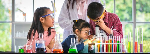 Naturwissenschaftler unterrichten asiatische Studenten im Laborraum, Junge schauen durch Mikroskop, buntes Reagenzglas und Mikroskop auf dem Tisch, Konzept für das Lernen im Laborraum. - Foto, Bild
