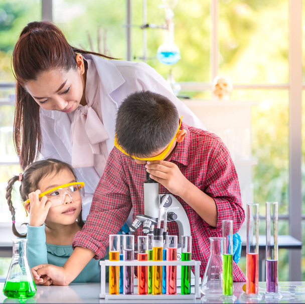 Science teacher teach Asian students in laboratory room, teacher look through microscope, colorful test tube and microscope on table , concept for study in laboratory room. - Photo, Image