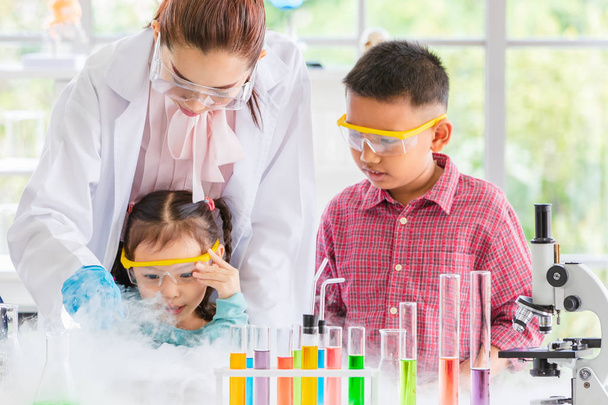 Science teacher teach Asian students in laboratory room, smoke float out of bowl, they excited, colorful test tube and microscope on table in laboratory room, concept for study in laboratory room. - Фото, зображення