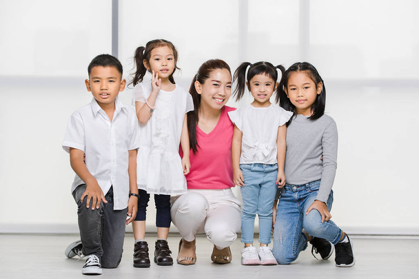 Smile Asian woman in pink shirt and Asian boy and girls squat on floor together, big white window behind them. - 写真・画像