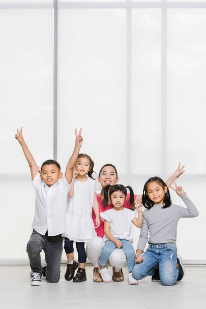 Sorriso donna asiatica in camicia rosa e ragazzo asiatico e ragazze squat sul pavimento insieme, grande finestra bianca dietro di loro
. - Foto, immagini