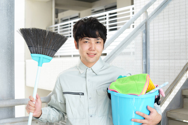 lächelnder asiatischer Hausmeister posiert mit Putzmitteln - Foto, Bild