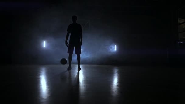 Basketbalspeler de bal in het licht van de lampen achter staat in de Doema schijnt klopt en klopt de bal op de vloer in de Basketbalhal in slow motion - Video