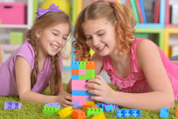 Cute girls playing with colorful plastic blocks on floor in room - Photo, Image