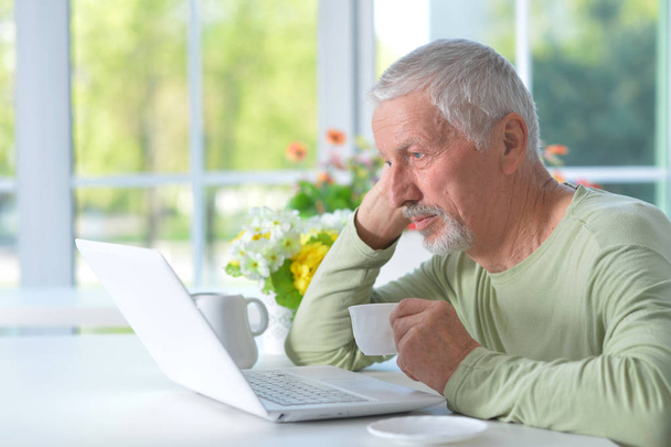  senior man using laptop while drinking tea at home - Фото, изображение