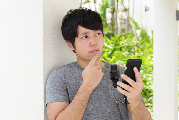 Ongemakkelijke Aziatische man met een slimme telefoon - Foto, afbeelding