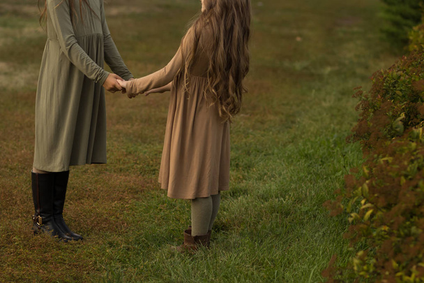 duas meninas estão de mãos dadas, amizade, brincar, andar no parque, forest.in um vestido marrom e verde
 - Foto, Imagem