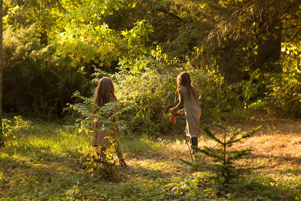 Kaksi tyttöä ruskeassa ja vihreässä mekossa juoksentelemassa ympäri metsää. Aurinko paistaa.
. - Valokuva, kuva
