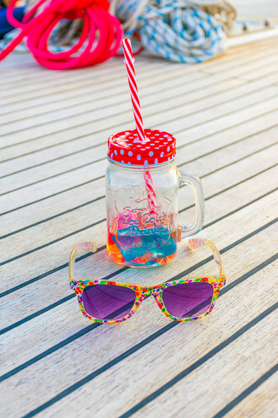 Luxurious purple glasses and unusual mug with straw on deck of yacht during journey. - Photo, Image