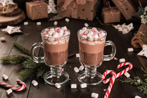 Xícara de chocolate quente bebida de cacau com um marshmallows e cana-de-açúcar na mesa de madeira. Dois copos de uma bebida de inverno doce e ramo de abeto
.  - Foto, Imagem