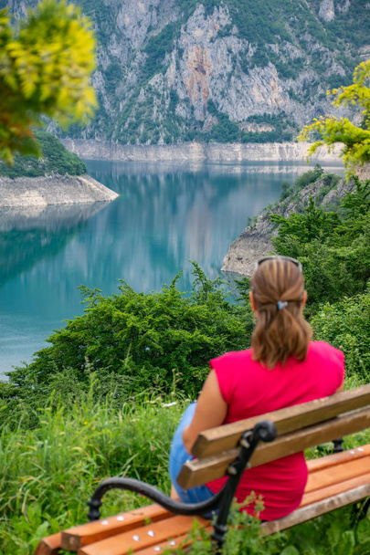 girl resting on bench near shore of mountain lake - Foto, imagen