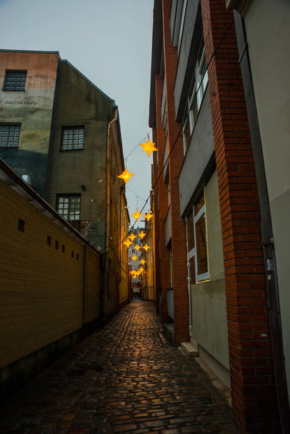 Narrow Rozena street in old town Riga, Latvia with stars garland. Christmas decoration on the european street. Rozena iela - Zdjęcie, obraz