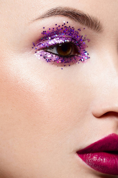 Close-up of the beauty of half a woman's face with creative fashionable make-up of sparkles. Black eyeliner and long eyelashes decorate hazel eyes and lips to match. Well-groomed skin after spa - Фото, зображення