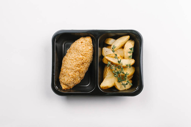 Ansicht der richtigen Ernährung mit gebratenen Kartoffeln und Sesam gebackenem Fleisch in Schachtel auf weißem Hintergrund - Foto, Bild