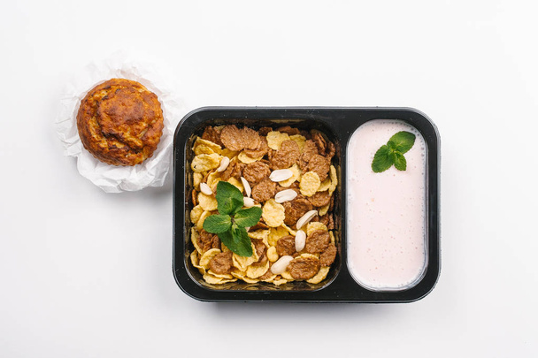 Draufsicht der richtigen Ernährung mit Joghurt und Cornflakes in Schachtel mit Cupcake auf weißem Hintergrund - Foto, Bild