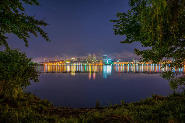 Colorido reflejo de ciudad resplandeciente en amplio río tranquilo
 - Foto, Imagen