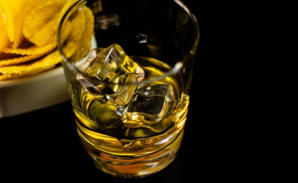 vaso de whisky con cubitos de hielo y aperitivos salados en el fondo de la barra, tiempo de fiesta
 - Foto, Imagen