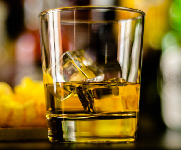 glass of whiskey with ice cubes and salty snacks on the background of the bar, party time - Photo, Image