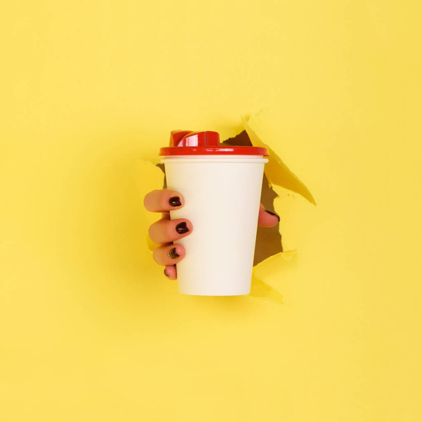 Female hand holding white paper mug on yellow background. Take away coffee cup concept. Mock up with copy space. Square crop - Foto, Imagem