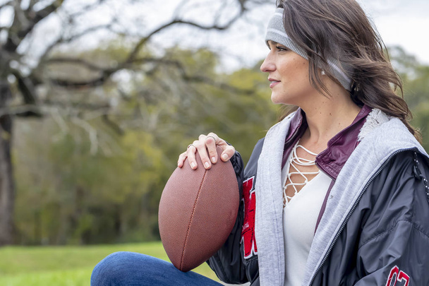 A beautiful Brunette model posing outdoors in an urban environment with a football - Photo, Image