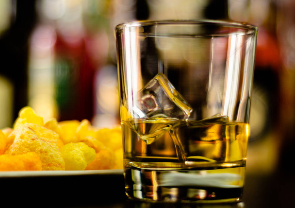 bardak viski buz küpleri ve bar, arka plan üzerinde tuzlu atıştırmalıklar ile parti zamanı - Fotoğraf, Görsel