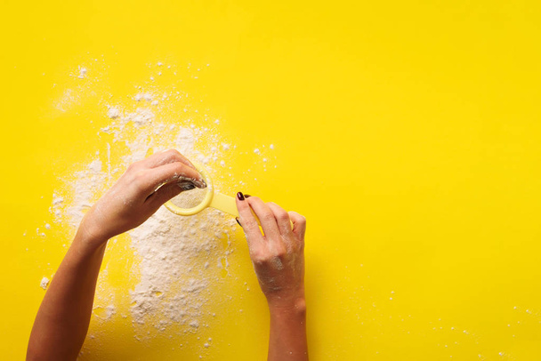Female hand holding sieve flour on yellow background. Baking and cooking concept. Banner with copy space. - Fotó, kép