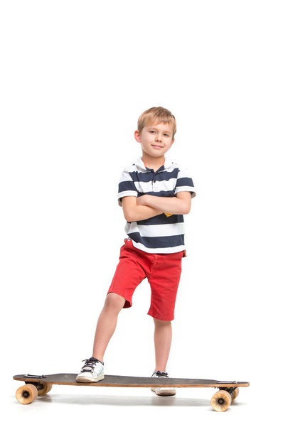 Full length portrait of an adorable young boy riding a skateboard isolated against white background - Фото, зображення