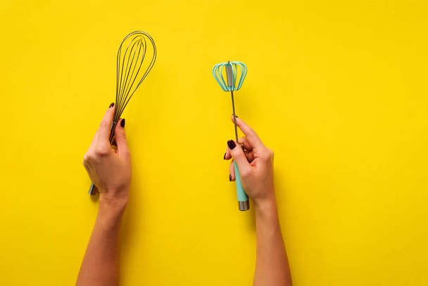 黄色の背景に女性の手の台所用品を保持。ベーキングツール-ブラシ、泡立て器、へら。ベーカリー、料理、健康的な自家製食品のコンセプト。スペースのコピー - 写真・画像