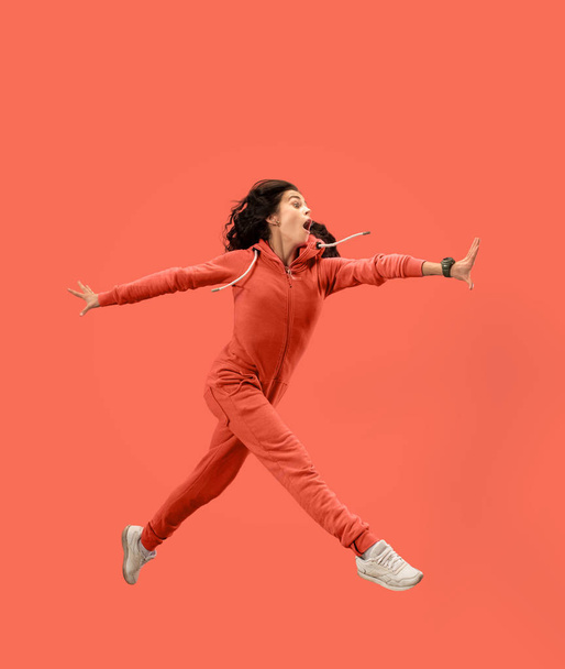 Freedom in moving. Pretty young woman jumping against coral background - Foto, afbeelding