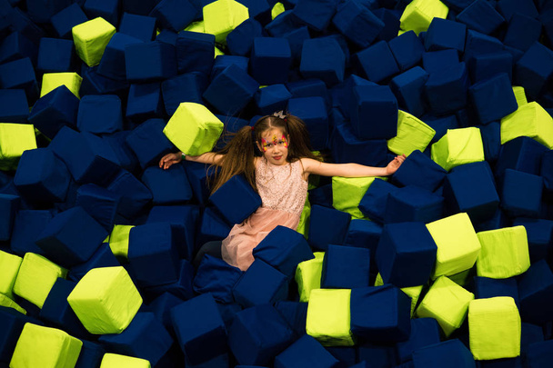 Meisje met plezier in een droge pool met lichte zachte kubussen te springen in. Kinderen spelen kamer - Foto, afbeelding