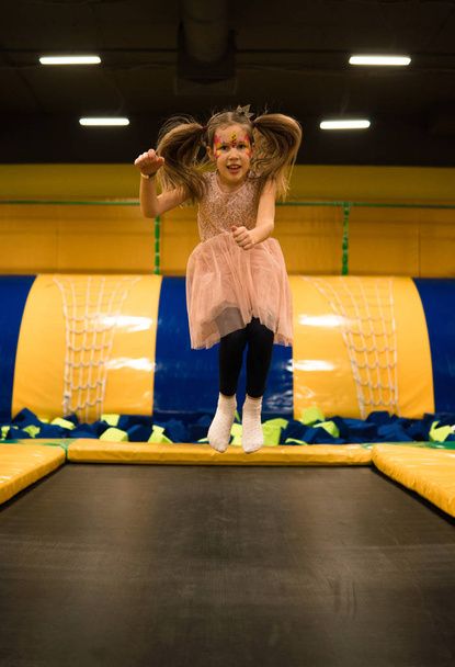 Little girl is jumping on a trampoline in kids play room on her birthday - Photo, Image