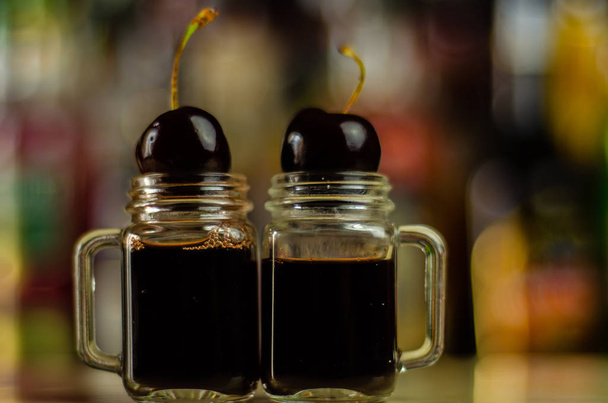 Licor de cereja e suculentas cerejas maduras na mesa do bar, uma elegante porção de bebida doce no restaurante, uma bebida tradicional.
 - Foto, Imagem