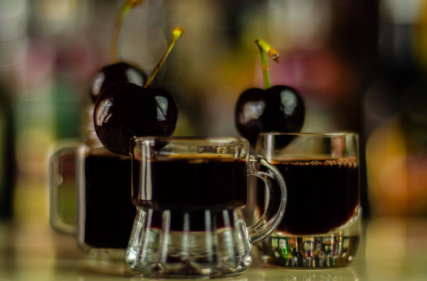 Λικέρ κεράσι και ζουμερά κεράσια ώριμα πάνω στο τραπέζι στο μπαρ, ένα κομψό σερβίρισμα γλυκών ποτών στο εστιατόριο, ένα παραδοσιακό ποτό - Φωτογραφία, εικόνα