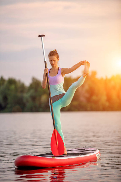 Mulher esportiva na posição de ioga no paddleboard, fazendo ioga no quadro de refeições, exercício para flexibilidade e alongamento dos músculos
 - Foto, Imagem
