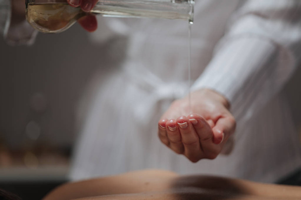 Massagista derramando óleo de massagem em sua mão em um centro de spa
. - Foto, Imagem
