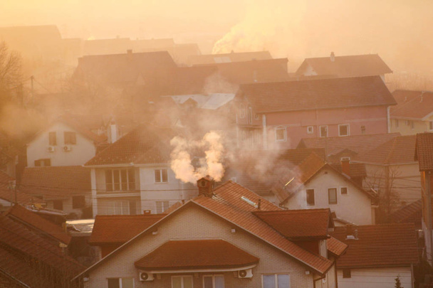 Курильні димоходи на дахах будинків випромінюють дим, дим на сході сонця, забруднювачі входять в атмосферу. Екологічна катастрофа. Шкідливі викиди та вихлопні гази в повітря. Туман, зимовий день, опалювальний сезон
. - Фото, зображення