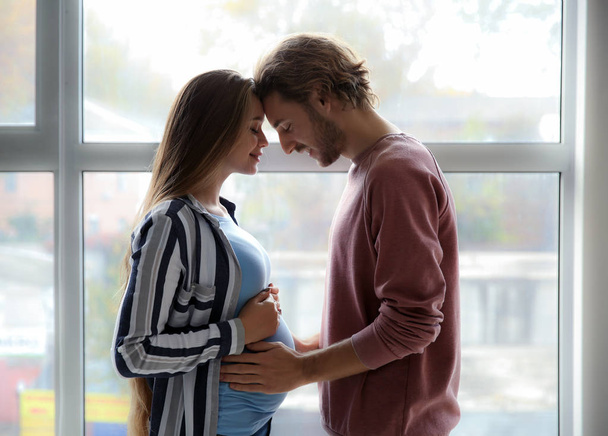 Giovane coppia incinta vicino alla finestra a casa
 - Foto, immagini