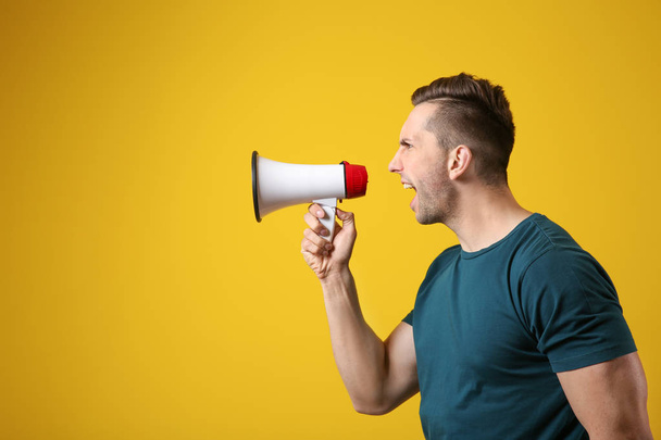 Screaming young man with megaphone on color background - Foto, imagen