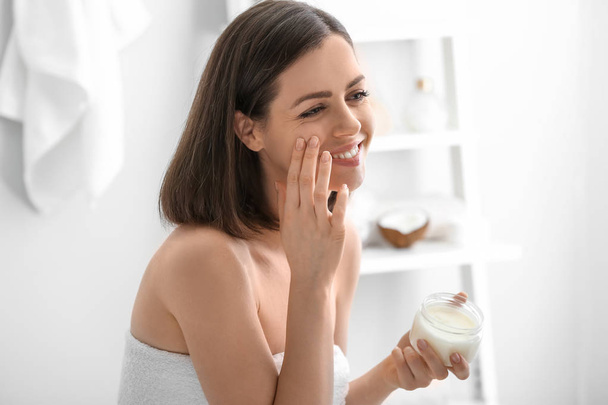Young woman applying coconut oil in bathroom - Photo, Image