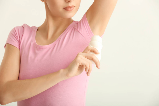 Mooie jonge vrouw met deodorant op lichte achtergrond - Foto, afbeelding