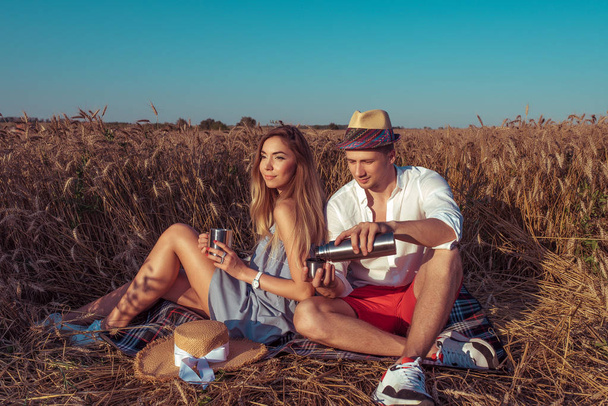 The guy with the girl in field is poured in a thermos in a mug not tea or coffee. Holiday in nature romantic pleasure in the evening. The concept of in love with a pair of wheat field. - Foto, Bild